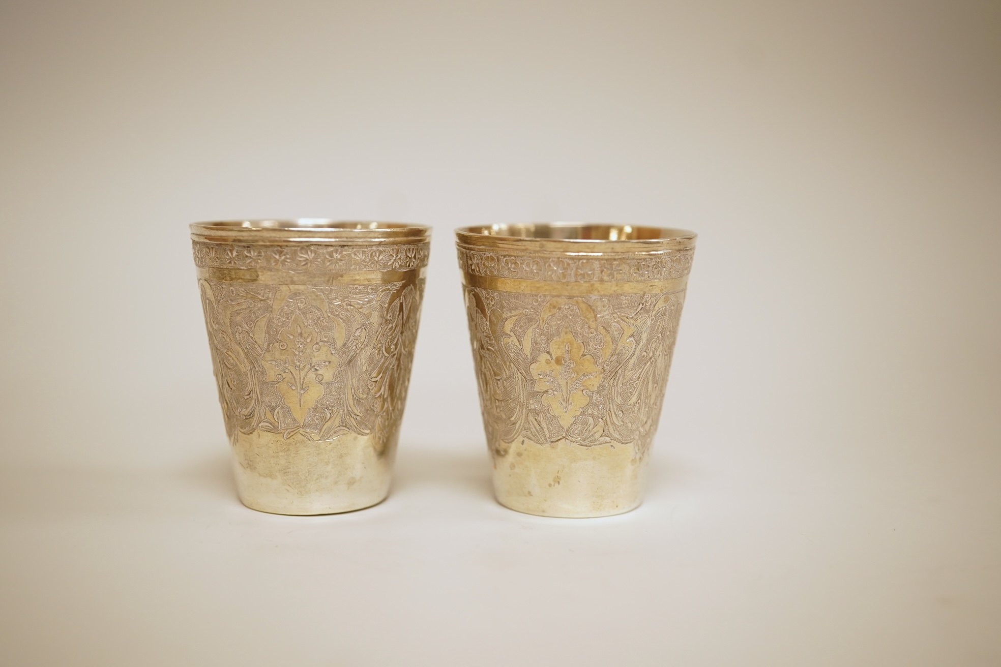 A set of six 20th century Middle Eastern white metal tots, 42mm and matching tray, 25.2cm, all engraved with geometric foliate decoration.